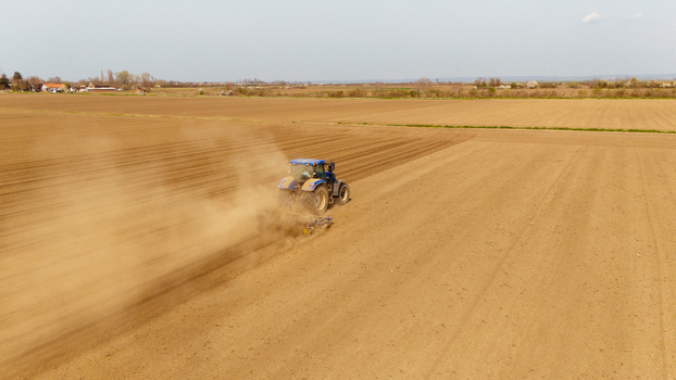 Aerial view of a blue tractor tilling the dry brown earth kicking up dust under a pale sky Sremska Mitrovica Vojvodina Serbia. Aerial view of a blue tractor tilling the dry brown earth kicking up dust under a pale sky Sremska Mitrovica Vojvodina Serbia.