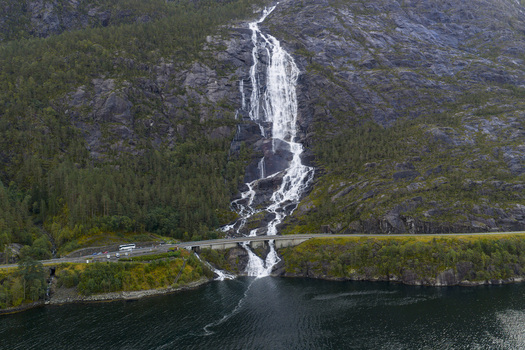 Aerial view of Langfossen waterfall cascading down a steep rocky cliff into the Akrafjorden with a road bridge at its base surrounded by dense green forest Fjaera Vestland Norway. Aerial view of Langfossen waterfall cascading down a steep rocky cliff into the Akrafjorden with a road bridge at its base surrounded by dense green forest Fjaera Vestland Norway.