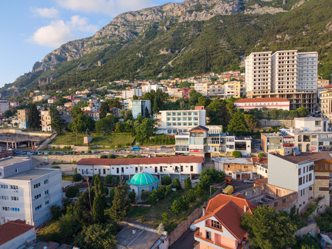Aerial view of the town featuring a turquoise domed mosque residential buildings and lush greenery at the foot of a rugged mountain in Kruje Durres County Albania.