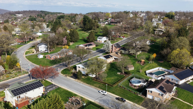 Aerial view of a suburban neighborhood featuring residential houses with solar panels green lawns swimming pools and tree lined streets in Akron Pennsylvania United States.