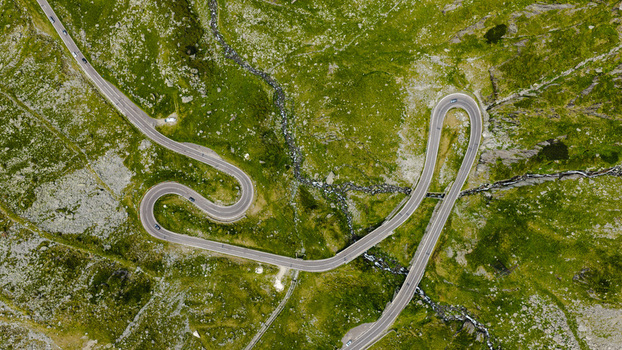 Aerial view of the winding Transfagarasan mountain road with sharp hairpin turns cutting through lush green alpine meadows in Curtea de Arges Judetul Arges Romania. Aerial view of the winding Transfagarasan mountain road with sharp hairpin turns cutting through lush green alpine meadows in Curtea de Arges Judetul Arges Romania.