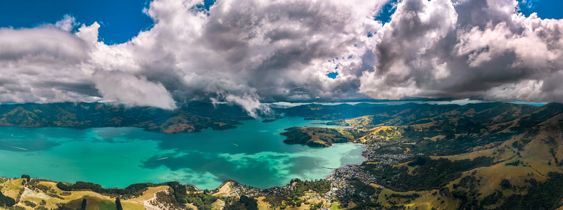 Aerial view of the turquoise waters of Akaroa Harbour surrounded by rolling green hills and dramatic clouds in Akaroa Canterbury Region New Zealand. Aerial view of the turquoise waters of Akaroa Harbour surrounded by rolling green hills and dramatic clouds in Akaroa Canterbury Region New Zealand.