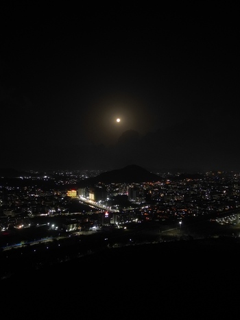 Aerial view of the full moon shining over the illuminated city skyline and dark hills at night in Mumbai Maharashtra India.