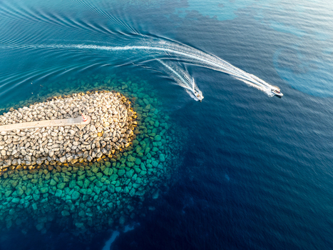 Aerial view of boats gliding across the turquoise waters near the rocky breakwater of Mgarr Harbour Gozo Malta.