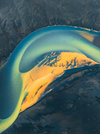 Aerial view of a vibrant turquoise glacial river winding through a dark volcanic landscape with golden sandbanks in Iceland. Aerial view of a vibrant turquoise glacial river winding through a dark volcanic landscape with golden sandbanks in Iceland.