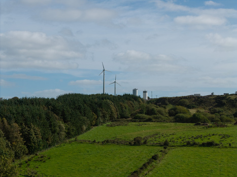 Aerial view of wind turbines rising above a lush green landscape with dense tree lines and rolling fields under a cloudy blue sky in Lisburn Northern Ireland United Kingdom. Aerial view of wind turbines rising above a lush green landscape with dense tree lines and rolling fields under a cloudy blue sky in Lisburn Northern Ireland United Kingdom.