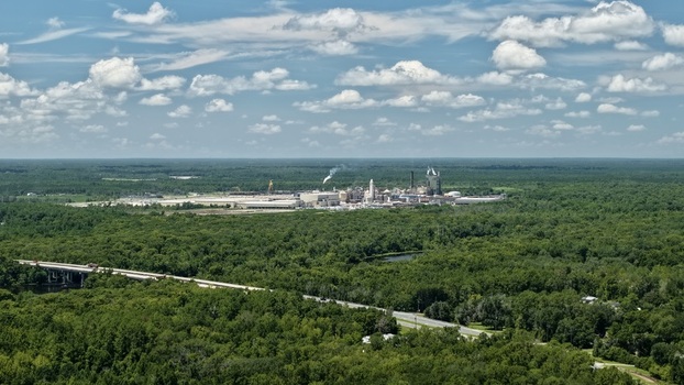 Aerial view of the Seminole Electric power plant with industrial fuel tanks surrounded by dense green forests and a highway bridge under a blue sky in Palatka Florida United States.