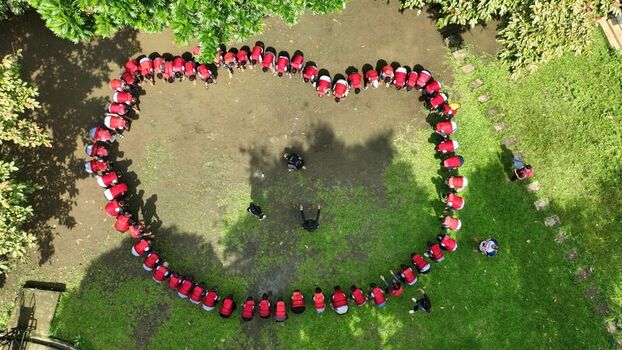 Aerial view of a group of people in red shirts forming a large heart shape on a clearing surrounded by lush green trees in Pangandaran West Java Indonesia. Aerial view of a group of people in red shirts forming a large heart shape on a clearing surrounded by lush green trees in Pangandaran West Java Indonesia.
