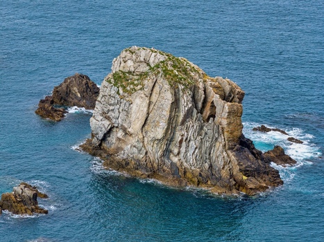 Aerial view of the jagged rock formations at Silence Beach Viewpoint surrounded by deep blue ocean water and smaller rocky outcrops in Cudillero Asturias Spain.