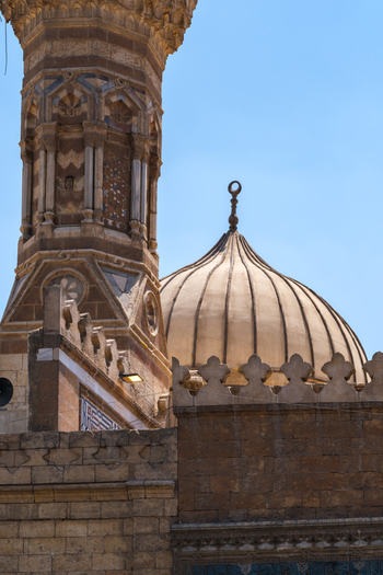 View of the Al Azhar Mosque featuring intricate stone carvings on the minaret and a ribbed dome under a clear blue sky in Cairo Egypt. View of the Al Azhar Mosque featuring intricate stone carvings on the minaret and a ribbed dome under a clear blue sky in Cairo Egypt.
