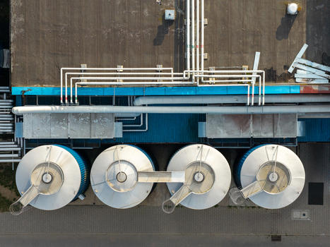Aerial view of raw milk storage tanks at a dairy processing facility featuring industrial piping and metal silos on a flat roof in Poland.
