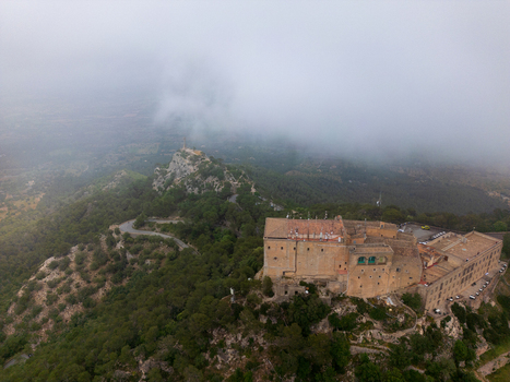 Aerial view of the Sanctuary of Sant Salvador on a mountain peak surrounded by lush green forests and low clouds in Felanitx Illes Balears Spain. Aerial view of the Sanctuary of Sant Salvador on a mountain peak surrounded by lush green forests and low clouds in Felanitx Illes Balears Spain.
