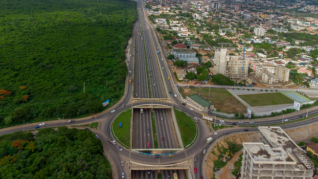 Accra Ghana 02 June 2023 Aerial view of Forever roundabout featuring a multi lane highway passing through the interchange bordered by dense urban development and lush forest.