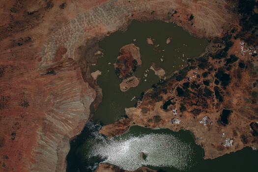 Aerial view of the reddish brown landscape featuring a green colored pond and excavated earth near the Kano Madobi Kiru Road in Watari Kano Nigeria. Aerial view of the reddish brown landscape featuring a green colored pond and excavated earth near the Kano Madobi Kiru Road in Watari Kano Nigeria.