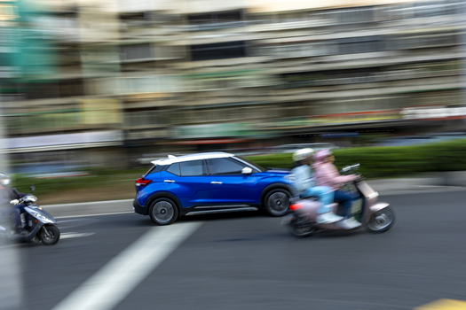 View of a blue SUV and scooters driving through a busy urban intersection with motion blur and city buildings in the background Taipei City Taiwan. View of a blue SUV and scooters driving through a busy urban intersection with motion blur and city buildings in the background Taipei City Taiwan.