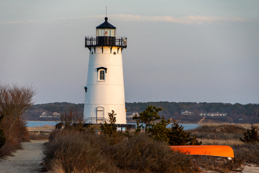 View of the Edgartown Harbor Light with its white tower and black lantern room surrounded by coastal shrubs and a sandy path in Edgartown Massachusetts United States.