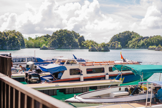 View of boats docked at a pier in a tropical bay with karst islands in the background Raja Ampat Southwest Papua Indonesia.