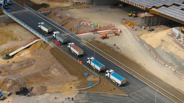 Aerial view of the Black Cat Roundabout highway construction site with trucks driving on a newly paved road and heavy machinery in Chawston England United Kingdom. Aerial view of the Black Cat Roundabout highway construction site with trucks driving on a newly paved road and heavy machinery in Chawston England United Kingdom.