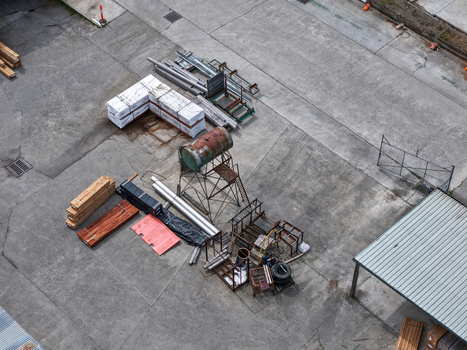 Melbourne VIC Australia 25 September 2026 Aerial view of an industrial yard featuring stacks of lumber metal pipes and a rusty water tank on a metal frame on concrete ground.