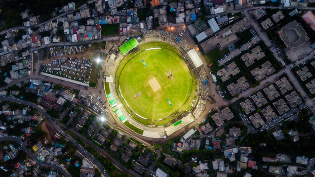 Aerial view of Muzaffarabad Cricket Stadium illuminated by floodlights surrounded by urban buildings and parked cars in Muzaffarabad Azad Kashmir Pakistan.