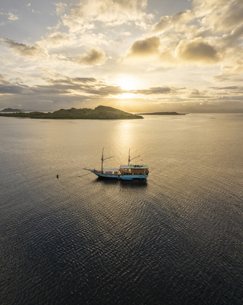 Aerial view of a traditional phinisi boat anchored in the calm waters near Komodo Island at sunset with golden light reflecting on the sea Komodo East Nusa Tenggara Indonesia.