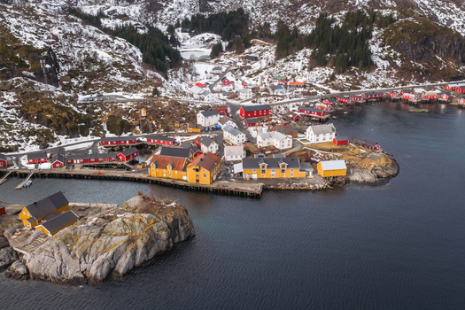 Aerial view of the charming fishing village with its vibrant red and yellow buildings nestled between the dark waters and snow dusted mountains Nusfjord Nordland Norway.