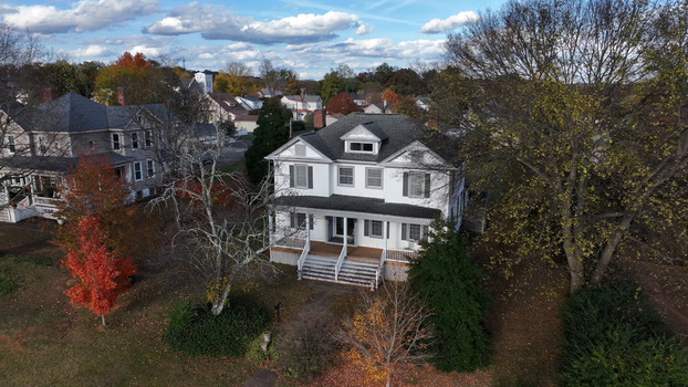 Aerial view of a white residential house with a front porch surrounded by autumn trees and a suburban neighborhood in Altavista Virginia United States. Aerial view of a white residential house with a front porch surrounded by autumn trees and a suburban neighborhood in Altavista Virginia United States.