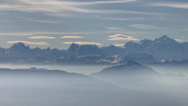 Aerial view of the majestic snow capped mountains piercing through a sea of ethereal fog casting long shadows across the undulating landscape Gex Auvergne Rhône Alpes France. Aerial view of the majestic snow capped mountains piercing through a sea of ethereal fog casting long shadows across the undulating landscape Gex Auvergne Rhône Alpes France.