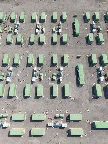 Aerial view of a Battery Energy Storage System installation with rows of green battery containers and electrical infrastructure on a gravel site in Tavazzano con Villavesco Lombardy Italy.