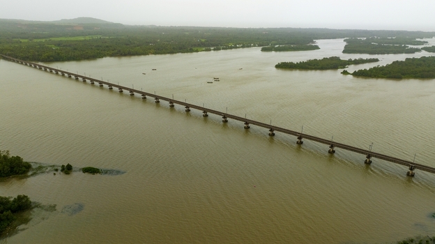 Aerial view of the long railway bridge spanning the Sharavathi River surrounded by lush green mangroves and calm water in Honnavar Karnataka India.