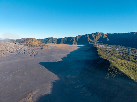 Aerial view of Mount Bromo volcanic landscape with the vast sand sea rugged crater rims and dramatic shadows under a clear blue sky in Sukapura East Java Indonesia. Aerial view of Mount Bromo volcanic landscape with the vast sand sea rugged crater rims and dramatic shadows under a clear blue sky in Sukapura East Java Indonesia.