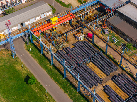 Aerial view of an industrial facility with a large orange gantry crane and stacks of metal pipes in an outdoor storage yard Kyjov South Moravian Region Czechia.