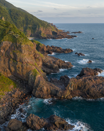 Aerial view of the rugged coastline featuring steep cliffs and rocky outcrops along the blue sea in Izu Shizuoka Japan. Aerial view of the rugged coastline featuring steep cliffs and rocky outcrops along the blue sea in Izu Shizuoka Japan.