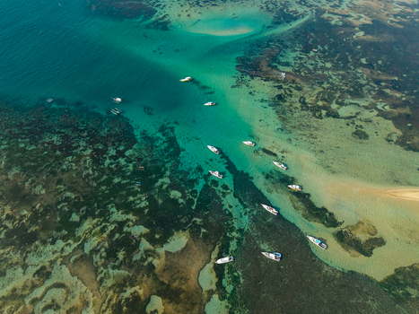 Aerial view of small boats anchored in the turquoise shallow waters over a vibrant coral reef in Kecamatan Denpasar Selatan Bali Indonesia.