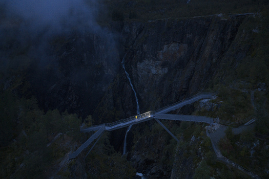 Aerial view of Voringfossen waterfall and the modern pedestrian bridge over a deep canyon at twilight with mist and a person on the walkway Eidfjord Municipality Vestland Norway.