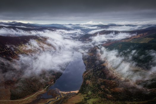 Aerial view of the glacial valley of Glendalough with mist rolling over the dark mountains and the Upper Lake under a moody sky in Glendalough County Wicklow Ireland.
