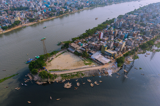 Aerial view of the Buriganga River with numerous traditional wooden boats docked along the shore and dense urban buildings in Keraniganj Dhaka Division Bangladesh. Aerial view of the Buriganga River with numerous traditional wooden boats docked along the shore and dense urban buildings in Keraniganj Dhaka Division Bangladesh.