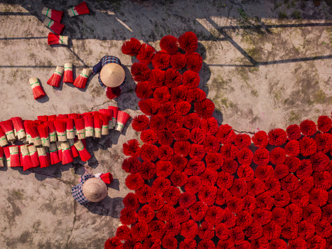 Aerial view of workers wearing conical hats arranging bundles of bright red incense sticks to dry on a concrete surface in Vietnam. Aerial view of workers wearing conical hats arranging bundles of bright red incense sticks to dry on a concrete surface in Vietnam.