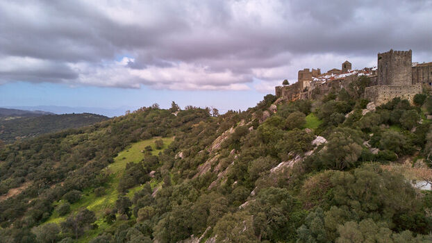 Aerial view of a medieval castle perched atop a verdant hill under a sky brushed with strokes of gray and pale blue Castellar de la Frontera Andalucía Spain. Aerial view of a medieval castle perched atop a verdant hill under a sky brushed with strokes of gray and pale blue Castellar de la Frontera Andalucía Spain.