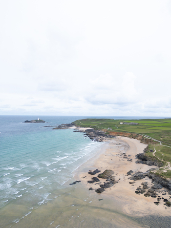 Aerial view of Godrevy Beach with turquoise waves sandy shores and the distant Godrevy Lighthouse under a cloudy sky in Gwithian England United Kingdom. Aerial view of Godrevy Beach with turquoise waves sandy shores and the distant Godrevy Lighthouse under a cloudy sky in Gwithian England United Kingdom.