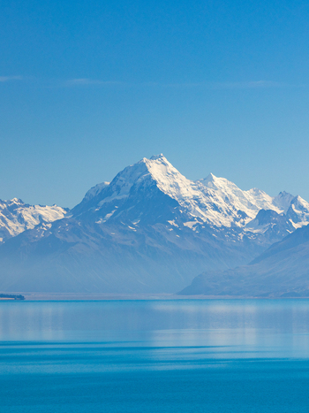 View of snow capped mountains mirroring in the tranquil azure lake under a clear blue sky creating a serene and breathtaking landscape Lake Pukaki Mount Cook Lookout New Zealand. View of snow capped mountains mirroring in the tranquil azure lake under a clear blue sky creating a serene and breathtaking landscape Lake Pukaki Mount Cook Lookout New Zealand.