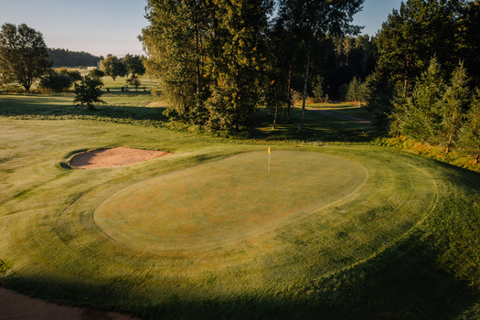 Aerial view of a golf course green with a sand bunker surrounded by lush trees and grass during golden hour in Valmiera Valmiera Latvija.