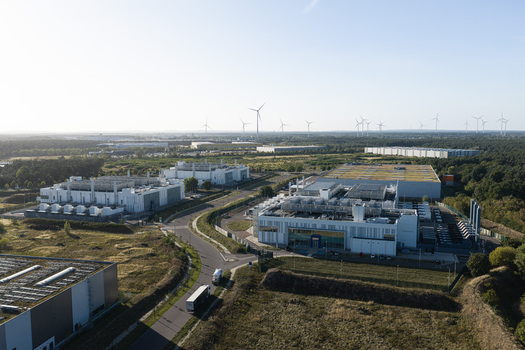 Aerial view of Vantage Data Centers BER1 facility with industrial buildings and rooftop cooling units near green fields and wind turbines in Ludwigsfelde Germany. Aerial view of Vantage Data Centers BER1 facility with industrial buildings and rooftop cooling units near green fields and wind turbines in Ludwigsfelde Germany.