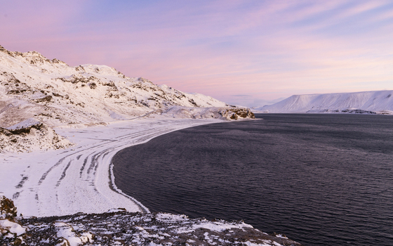View of snow covered mountains meet the tranquil dark waters under a pastel sky creating a peaceful contrast in Kleifarvatn Grindav&iacute;kurb&aelig;r Iceland.