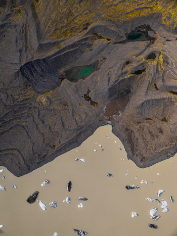 Aerial view of a glacial landscape featuring dark volcanic moraine turquoise meltwater pools and floating icebergs in silty water in Iceland. Aerial view of a glacial landscape featuring dark volcanic moraine turquoise meltwater pools and floating icebergs in silty water in Iceland.