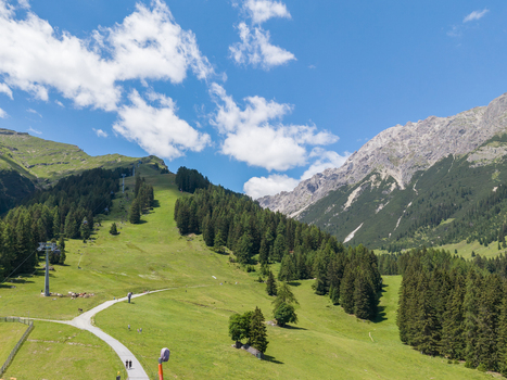 Aerial view of the alpine landscape in Imst featuring green mountain slopes a cable car line and a winding path under a bright blue sky in Imst Tyrol Austria.