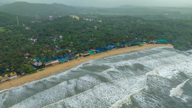 Aerial view of Palolem Beach with its crescent shaped coastline palm trees and small structures along the shore in Canacona Goa India.