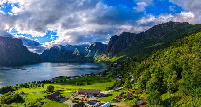 Aerial view of the village of Flam nestled between steep mountains and the Aurlandsfjord with lush green fields small wooden cabins and a dramatic cloudy sky in Flam Vestland Norway. Aerial view of the village of Flam nestled between steep mountains and the Aurlandsfjord with lush green fields small wooden cabins and a dramatic cloudy sky in Flam Vestland Norway.