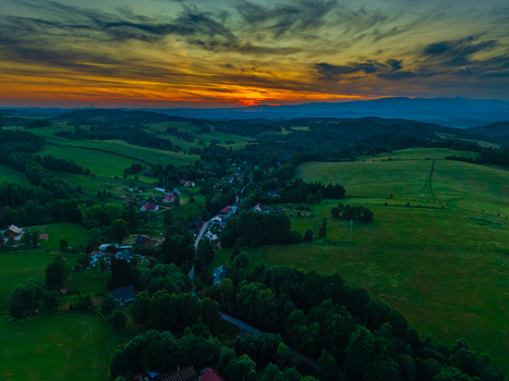 Aerial view of the village of Horni Zdar nestled among rolling green hills and lush forests under a vibrant sunset sky in Jindrichuv Hradec South Bohemian Region Czechia.