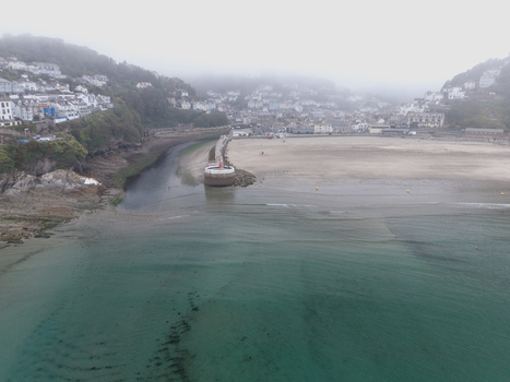 Aerial view of the sandy beach harbour entrance and historic buildings nestled along the hillside under a thick blanket of morning mist in Looe Cornwall United Kingdom. Aerial view of the sandy beach harbour entrance and historic buildings nestled along the hillside under a thick blanket of morning mist in Looe Cornwall United Kingdom.